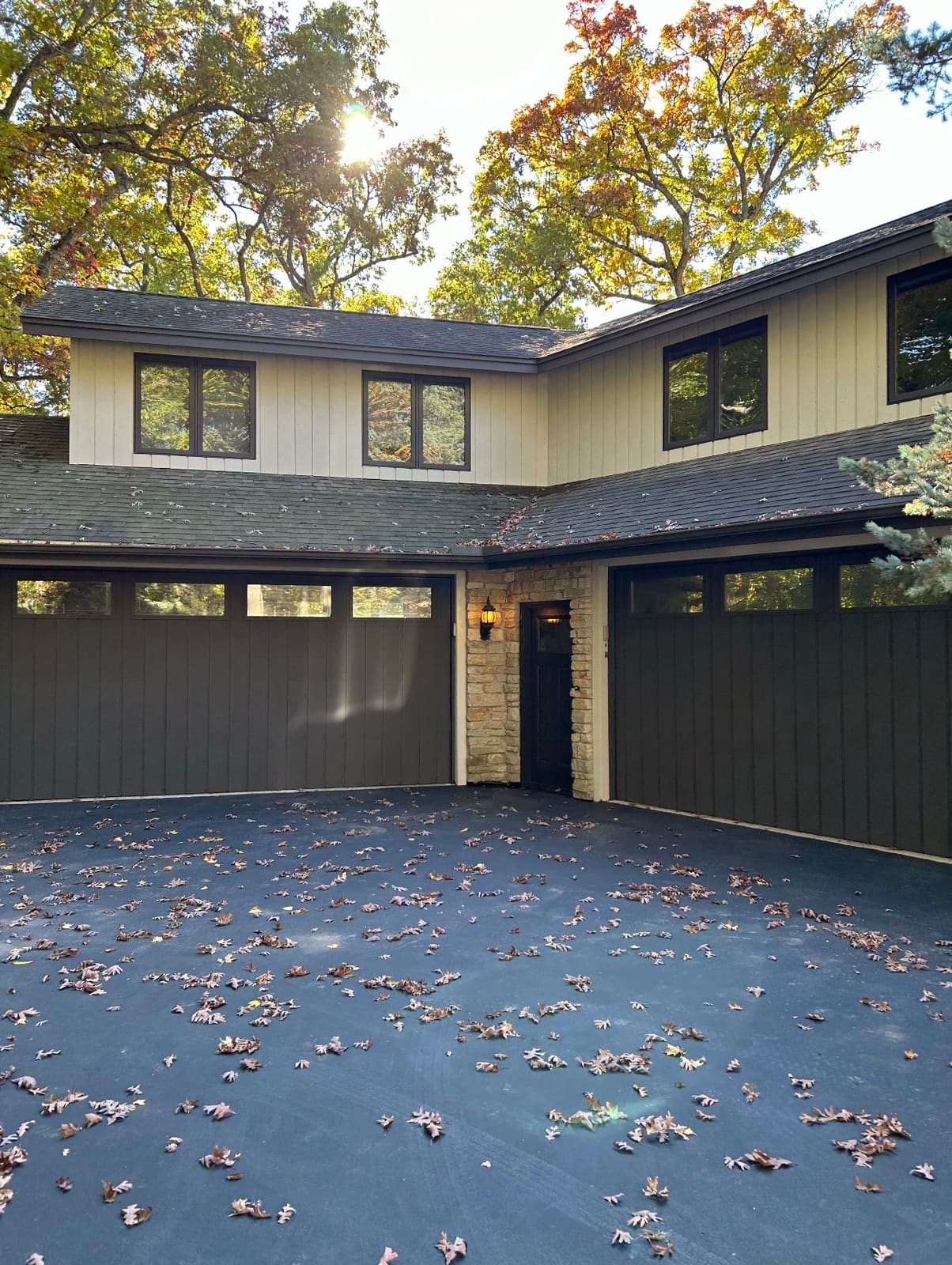Two-story home exterior painted in cream board-and-batten siding with black window trim, above two dark gray garage doors and a stone entry column