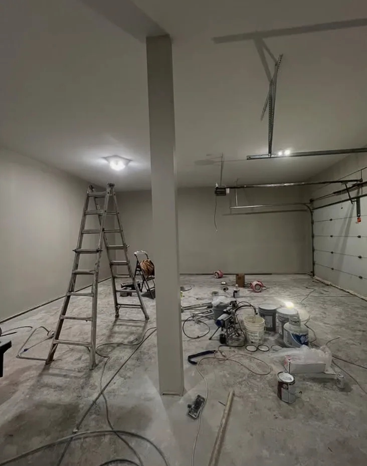 Attached garage interior with freshly finished and painted gray walls and ceiling, and a bare concrete floor ground and prepped for coating
