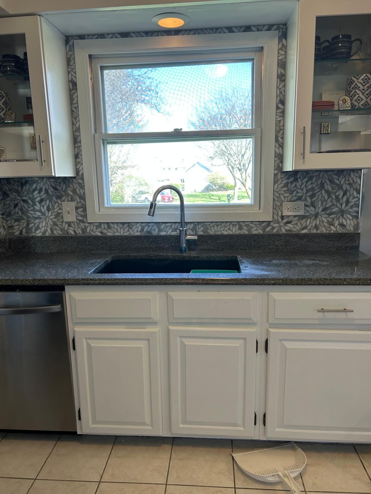 Kitchen sink run with white raised-panel cabinets, dark speckled granite countertop, black gooseneck pull-down faucet and a gray floral patterned tile backsplash under a window